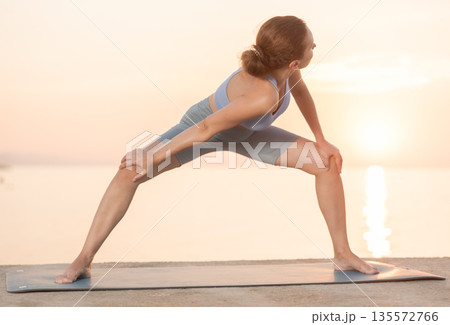 Near sea during sunset, girl performs variations of Himavanasana Near sea during sunset, girl performs variations of Himavanasana 135572766