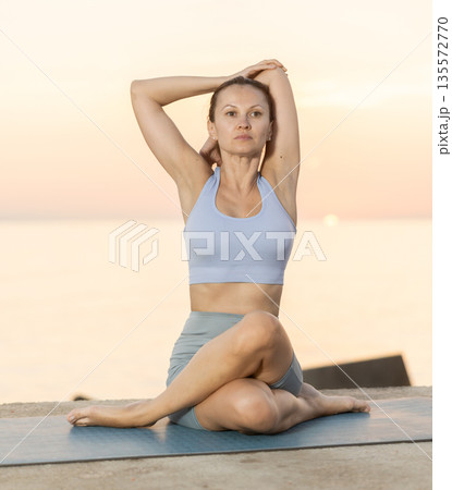 Young woman maintaining mental and physical health attending, practicing twisting yoga exercises on beach at morning Young woman maintaining mental and physical health attending, practicing twisting yoga exercises on beach at morning 135572770
