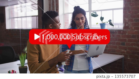 Collaborating coworkers pointing at silver laptop with red subscriber overlay in office with mug Collaborating coworkers pointing at silver laptop with red subscriber overlay in office with mug 135573707