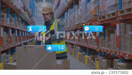 Warehouse worker in safety vest stacking cardboard box on pallet rack in aisle, with floating icons 135573802