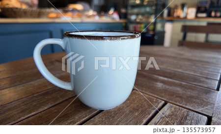 Coffee cup sits on a wooden table in a cafe setting 135573957