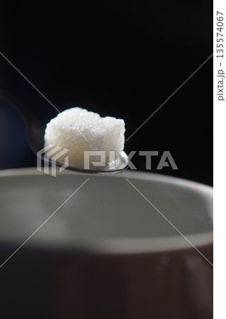 Spoon with sugar near a brown cup on a dark surface 135574067