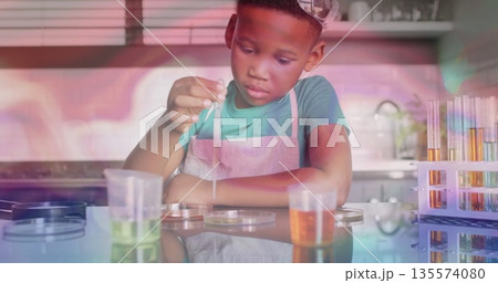 Boy wearing apron conducting experiment in kitchen, with dropper, petri dishes and test tubes 135574080