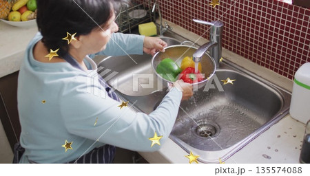 Rinsing Senior Indian woman holding metal colander at kitchen sink, cleaning colorful bell peppers Rinsing Senior Indian woman holding metal colander at kitchen sink, cleaning colorful bell peppers 135574088