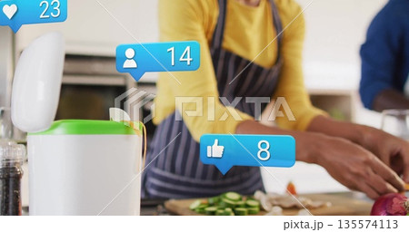 Couple wearing aprons chopping vegetables on cutting board, showing cucumbers and onion in kitchen 135574113
