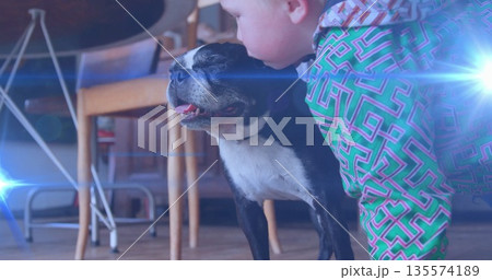 Kneeling toddler boy in patterned hoodie kissing dog beside chair in living room, copy space Kneeling toddler boy in patterned hoodie kissing dog beside chair in living room, copy space 135574189