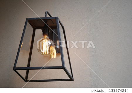 Elegant hanging lantern with warm light on plain wall 135574214