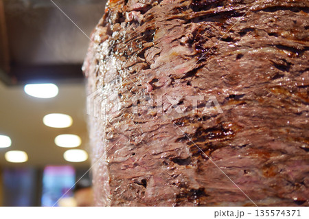 Juicy meat on a spit roasting in a lively street food setting Juicy meat on a spit roasting in a lively street food setting 135574371