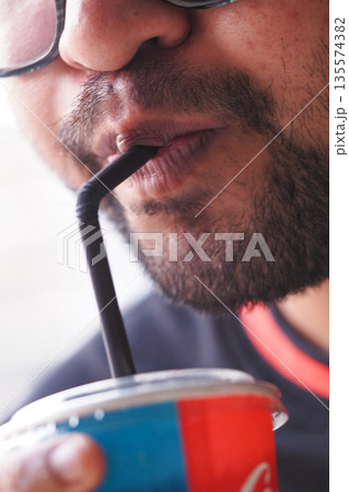 Enjoying a refreshing drink through a black straw in warm sunlight 135574382