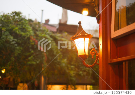 Warm street lamp illuminates cozy corner in rainy weather Warm street lamp illuminates cozy corner in rainy weather 135574430