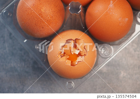 Egg with broken shell reveals yolk inside carton Egg with broken shell reveals yolk inside carton 135574504