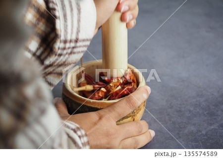 Hands grind spices in a wooden bowl with a pestle 135574589