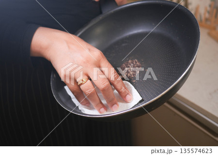 Cleaning a frying pan with paper towel in a kitchen Cleaning a frying pan with paper towel in a kitchen 135574623