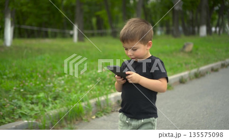 Little boy walking in park looking at smartphone screen 4k Little boy walking in park looking at smartphone screen 4k 135575098
