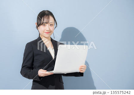 水色背景でパソコンを持つスーツの若い女性 新卒や就職のビジネスイメージ 就活の採用イメージカメラ目線 水色背景でパソコンを持つスーツの若い女性 新卒や就職のビジネスイメージ 就活の採用イメージカメラ目線 135575242