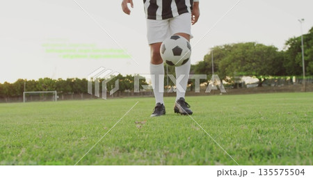Juggling male soccer player wearing jersey tapping soccer ball mid-air on grass with goalpost view Juggling male soccer player wearing jersey tapping soccer ball mid-air on grass with goalpost view 135575504