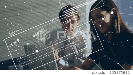 Two office professionals reviewing laptop screen with pen in office, with floating data panels 135575656