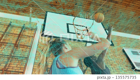 Reaching athlete in blue jersey shooting orange basketball at gym, with male opponent blocking hoop 135575735