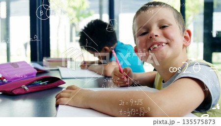 Smiling boy holding pencil and writing on notebooks and math sheets at classroom desk, copy space Smiling boy holding pencil and writing on notebooks and math sheets at classroom desk, copy space 135575873