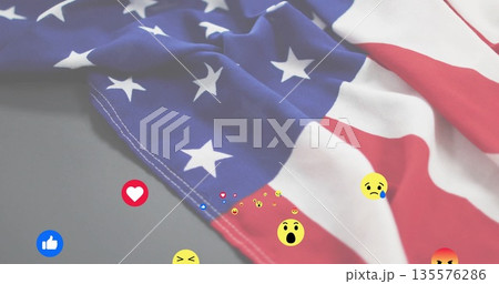 Draping folded American flag across smooth gray tabletop, with floating digital reaction icons 135576286