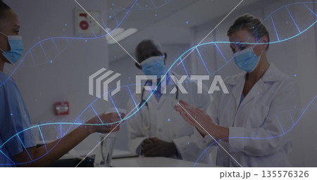 Medical team exchanging hand sanitizer in hospital corridor, wearing face masks, DNA helix graphics 135576326
