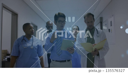 Walking healthcare team discussing rounds in hospital corridor with tablet, charts and stethoscopes 135576327