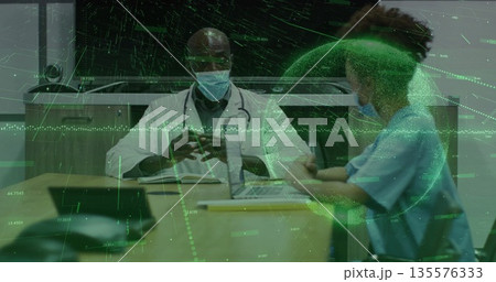 Discussing documents and plans at clinic desk in medical attire, with stethoscope and laptop 135576333