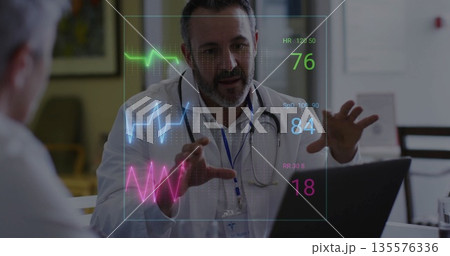 Gesturing doctor wearing coat, stethoscope consulting at clinic desk with laptop and vital graphs Gesturing doctor wearing coat, stethoscope consulting at clinic desk with laptop and vital graphs 135576336
