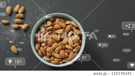 Displaying ceramic bowl holding almonds beside scattered almonds on tabletop, with overlay icons 135576345