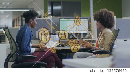 Collaborating pair viewing network graphic at desk behind partition, using laptops dual monitors 135576453
