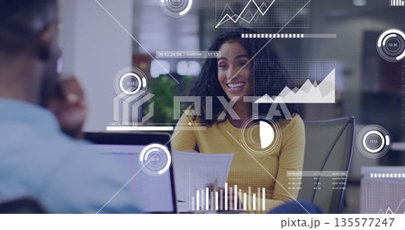 Presenting Hispanic woman holding printed reports at office desk, with laptop and data overlays 135577247