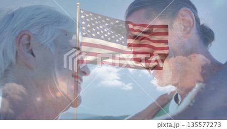 Smiling mother and son standing face to face on hilltop, with fluttering American flag on flagpole 135577273