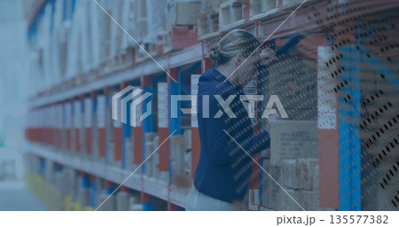 Leaning warehouse supervisor wearing suit inspecting box in warehouse, with metal racks, copy space Leaning warehouse supervisor wearing suit inspecting box in warehouse, with metal racks, copy space 135577382