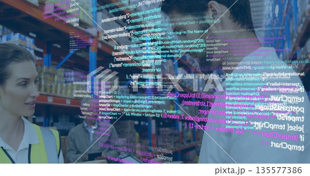 Warehouse team in vests reviewing process on warehouse floor, with tablet and digital code overlay 135577386