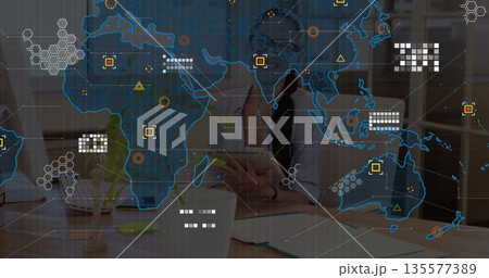 Holding tablet, woman in button-down shirt exploring network overlay at office desk, with monitor 135577389
