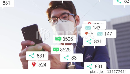 Masked Asian businessman holding smartphone, viewing alerts in business plaza, with chat overlays Masked Asian businessman holding smartphone, viewing alerts in business plaza, with chat overlays 135577424