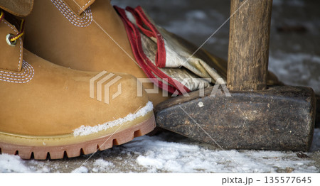 Work boots and sledgehammer resting on snowy ground, ready for winter labor Work boots and sledgehammer resting on snowy ground, ready for winter labor 135577645