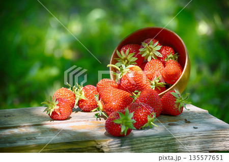 A bowl of fresh, ripe strawberries spills onto a wooden table. A bowl of fresh, ripe strawberries spills onto a wooden table. 135577651