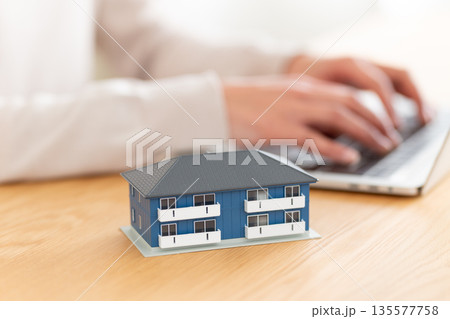 アパートの住宅模型とパソコンを操作するミドル女性の手元 135577758