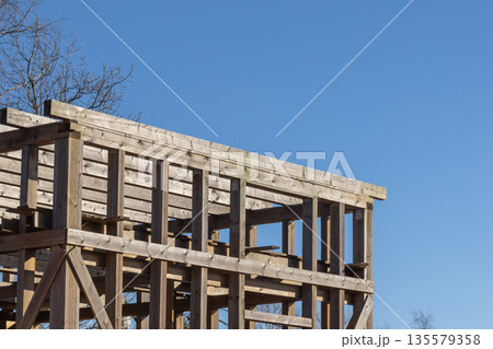 Timber frame construction rises with wooden scaffolding under a bright blue sky 135579358
