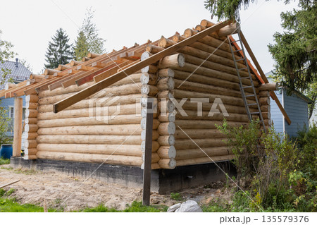 A partially built log cabin sits on a concrete foundation in a yard 135579376