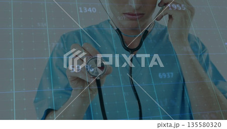Doctor holding stethoscope chest piece in clinic, wearing blue scrubs with digital grid overlay 135580320