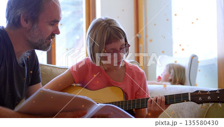 Strumming teen girl in eyeglasses playing acoustic guitar on home sofa, father guiding sheet music Strumming teen girl in eyeglasses playing acoustic guitar on home sofa, father guiding sheet music 135580430
