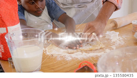Father and son in aprons kneading dough on kitchen countertop, with rolling pin and sprinkles Father and son in aprons kneading dough on kitchen countertop, with rolling pin and sprinkles 135580435