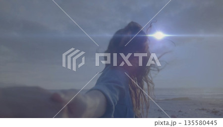 Holding partner hand, woman wearing denim shirt walking along sandy shore, sun flare sparkling Holding partner hand, woman wearing denim shirt walking along sandy shore, sun flare sparkling 135580445