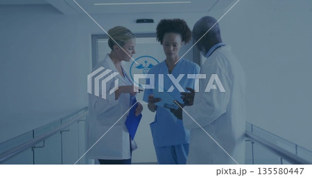 Reviewing paperwork staff wearing lab coats with blue folders in hospital corridor with door emblem Reviewing paperwork staff wearing lab coats with blue folders in hospital corridor with door emblem 135580447