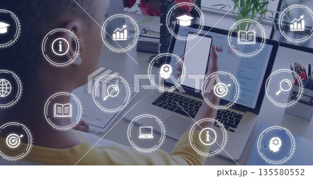 Man wearing mustard sweater holding phone, viewing laptop screen in office, data icons, copy space 135580552