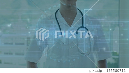 Standing female doctor monitoring digital interface inside clinic, with stethoscope and lab coat Standing female doctor monitoring digital interface inside clinic, with stethoscope and lab coat 135580711