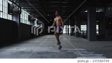 Skipping rope shirtless male exercising in industrial warehouse, wearing shorts and running shoes Skipping rope shirtless male exercising in industrial warehouse, wearing shorts and running shoes 135580749