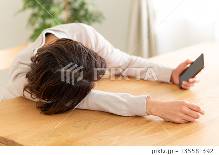 部屋でスマホを見てだらけるミドル女性 135581392